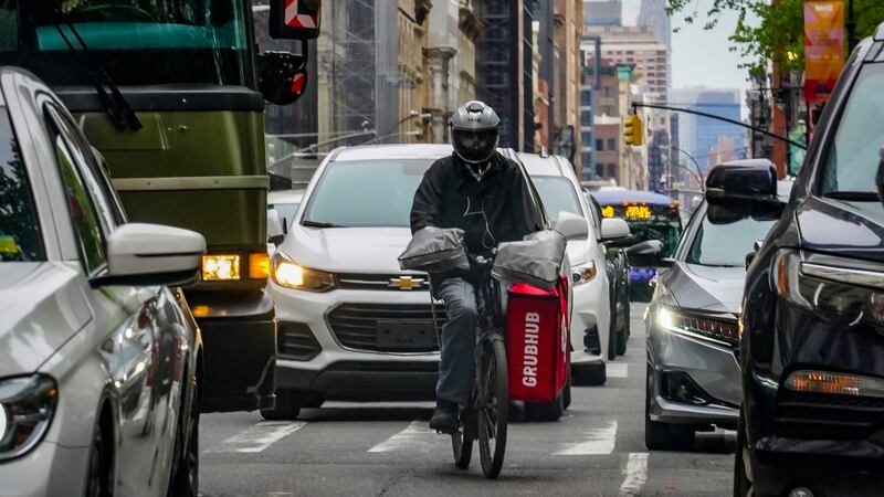 FILE - A food delivery worker rides through a busy street in lower Manhattan, Friday, April...